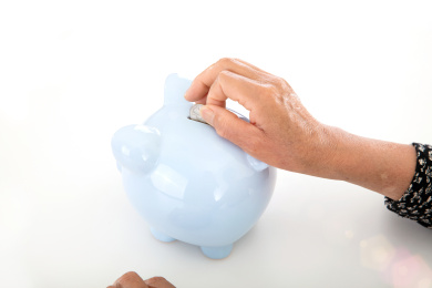 一位黄皮肤老年人手拿美元硬币投入小猪存钱罐中