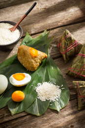箬叶上放着糯米和蛋黄粽子，旁边放着粽子食材