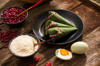 黑色盘子里放着三个新鲜的尖角粽子，旁边放着粽子食材