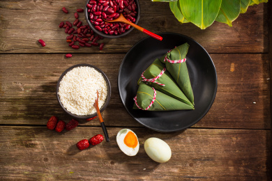 黑色盘子里放着三个新鲜的尖角粽子，旁边放着粽子食材