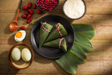 黑色盘子里放着三个新鲜的尖角粽子，旁边放着粽子食材