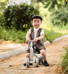 阳光下林荫小路上穿着短袖西服坐在滑滑车上开心的小男孩