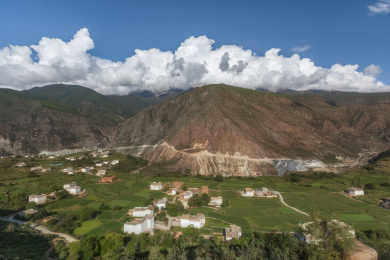 晴天蓝天白云下的四川甘孜州乡城县郊区绿色农田里的藏族村落