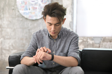 坐在沙发上的黄皮肤年轻男士正在查看戴在手上的商务手环