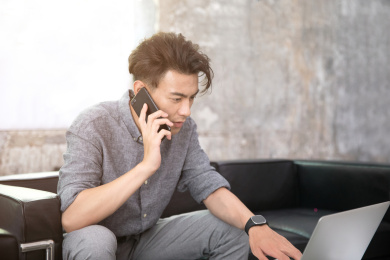 坐在沙发上边打电话边操作笔记本电脑的商务男性