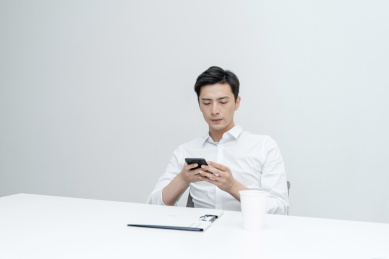 坐在办公桌看着手机的年轻男性