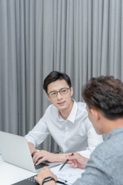 在白色办公桌和银色笔记本电脑前讨论工作的两位年轻男性白领