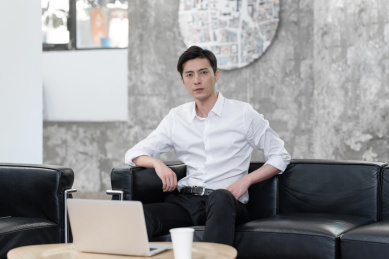 坐在黑色沙发上使用笔记本电脑的年轻男性白领