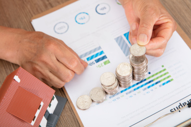 老者手拿硬币正在码放金融文件上递增的房款及旁边一个小房子模型