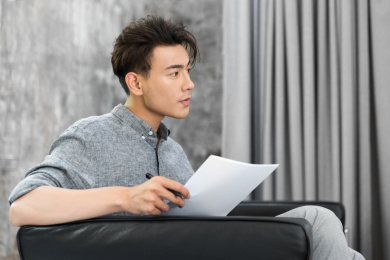 一名年轻的亚裔男手拿资料坐在沙发上