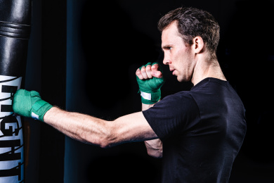 黑色背景特写肌肉线条清晰的男性手上缠着拳击绷带在打沙包