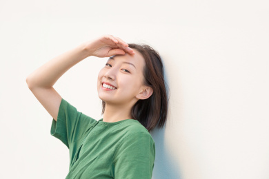 单手放在额头上遮挡阳光的亚裔女人在纯色背景墙前