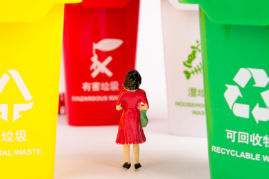 一个小人模型被不同类型的垃圾桶包围在中间，正在思考垃圾分类的事情