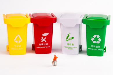 一个小人模型站在一排垃圾桶模型前面，正在思考垃圾分类的事情