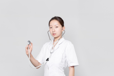 一名站在灰色背景墙前手持听诊器的女医生看向镜头