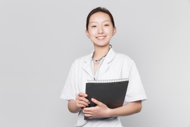 一位年轻美丽的女医生手拿资料站在灰色背景前面带微笑