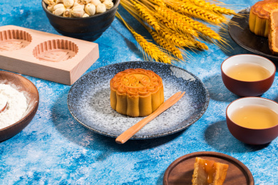 放在盘子里的一个中式流心月饼，周围摆这茶杯和食材