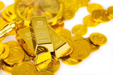 麻布背景上无序摆放着的金条金币和放大镜