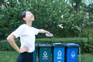 一个年轻的亚裔女孩手拿塑料瓶指向垃圾分类箱