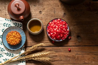 古旧木纹桌子上摆放着月饼和茶壶还有石榴