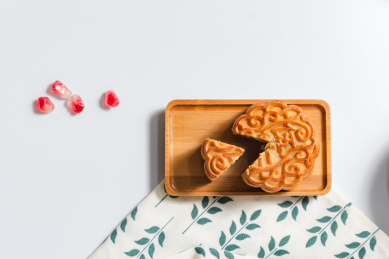 白底上长方形竹盘里装着的一个切开一角的月饼和几粒石榴籽