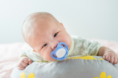 白色背景前趴在软垫上的初生婴儿和安抚奶嘴