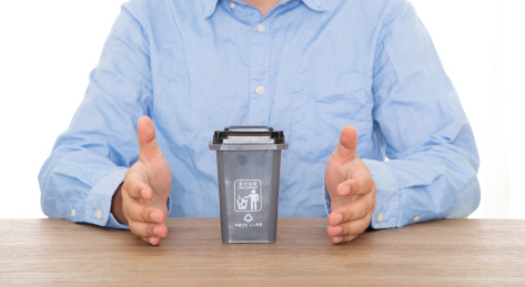 穿着蓝色衬衣的男性双手呵护着桌子上其它垃圾垃圾桶模型