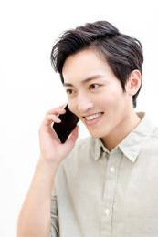 一位亚洲男性白领坐在工位上拿着手机打电话