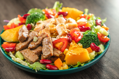 暗色木纹桌面上放着一盘煎鸡腿肉和牛肉条的蔬菜沙拉