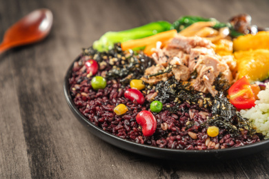 暗色木纹桌面上放着一盘金枪鱼南瓜黑米饭简餐