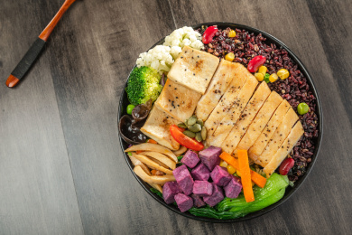 暗色木纹桌面上放着一盘煎鸡胸肉豆腐块黑米饭简餐