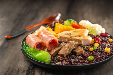 暗色木纹桌面上放着一盘煎牛肉条与鸡胸肉培根黑米饭简餐
