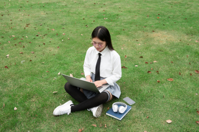 黄色人种青年学生在草地上用笔记本电脑认真学