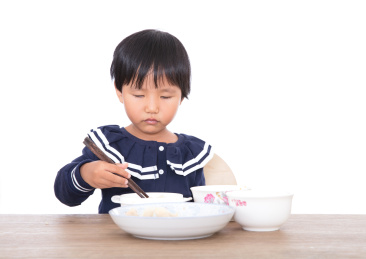 白背景前的三岁黄皮肤女孩在独自吃饭