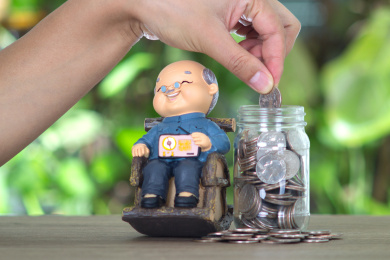 手拿美元硬币放进坐着摇椅老爷爷模型旁的玻璃瓶里