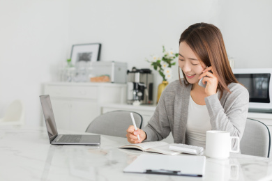 年轻女性在家坐在餐坐前一边工作一边使用手机