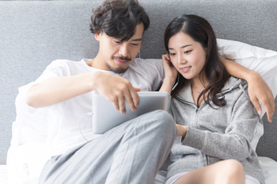 一对情侣在床上戴着耳机使用平板电脑