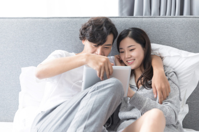 一对情侣靠在床头戴着耳机使用平板电脑