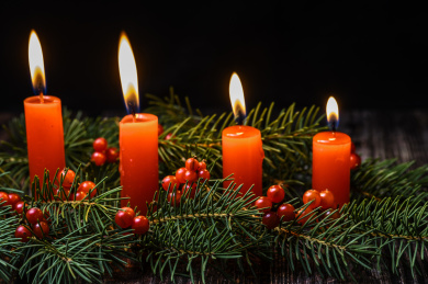 摆放在木质桌面上的圣诞树、红浆果和燃烧中的红色蜡烛