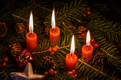 摆放在木质桌面上的圣诞树、红浆果和燃烧中的红色蜡烛