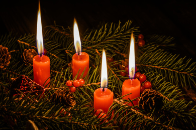 摆放在木质桌面上的圣诞树、红浆果和燃烧中的红色蜡烛