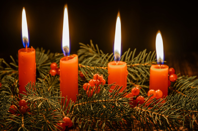 摆放在木质桌面上的圣诞树、红浆果和燃烧中的红色蜡烛