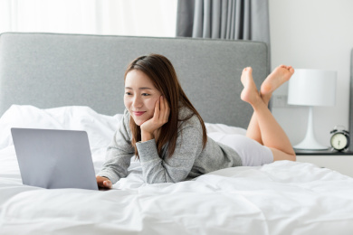 白天一个年轻女性在卧室的床上玩电脑