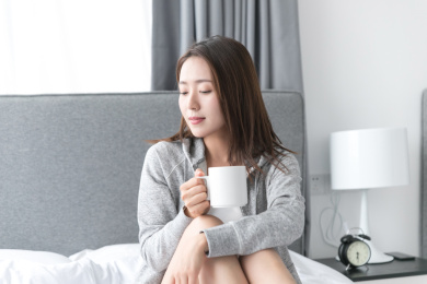 一名年轻女性坐在卧室床上喝水