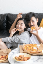 一对情侣在客厅沙发旁吃披萨