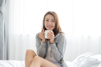 一名年轻女性坐在床上拿着水杯喝水