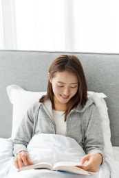 一个年轻女性坐在床上低头看书