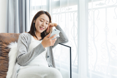 年轻女性在家烤着沙发使用手机听音乐