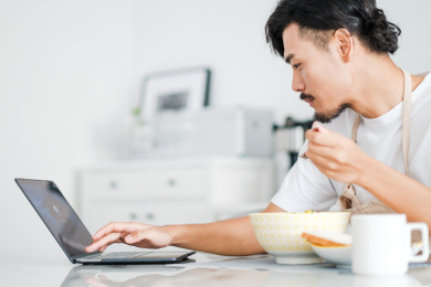 年轻男人在家里一边吃早饭一边看电脑