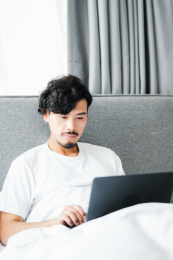 年轻男人坐在床上使用电脑